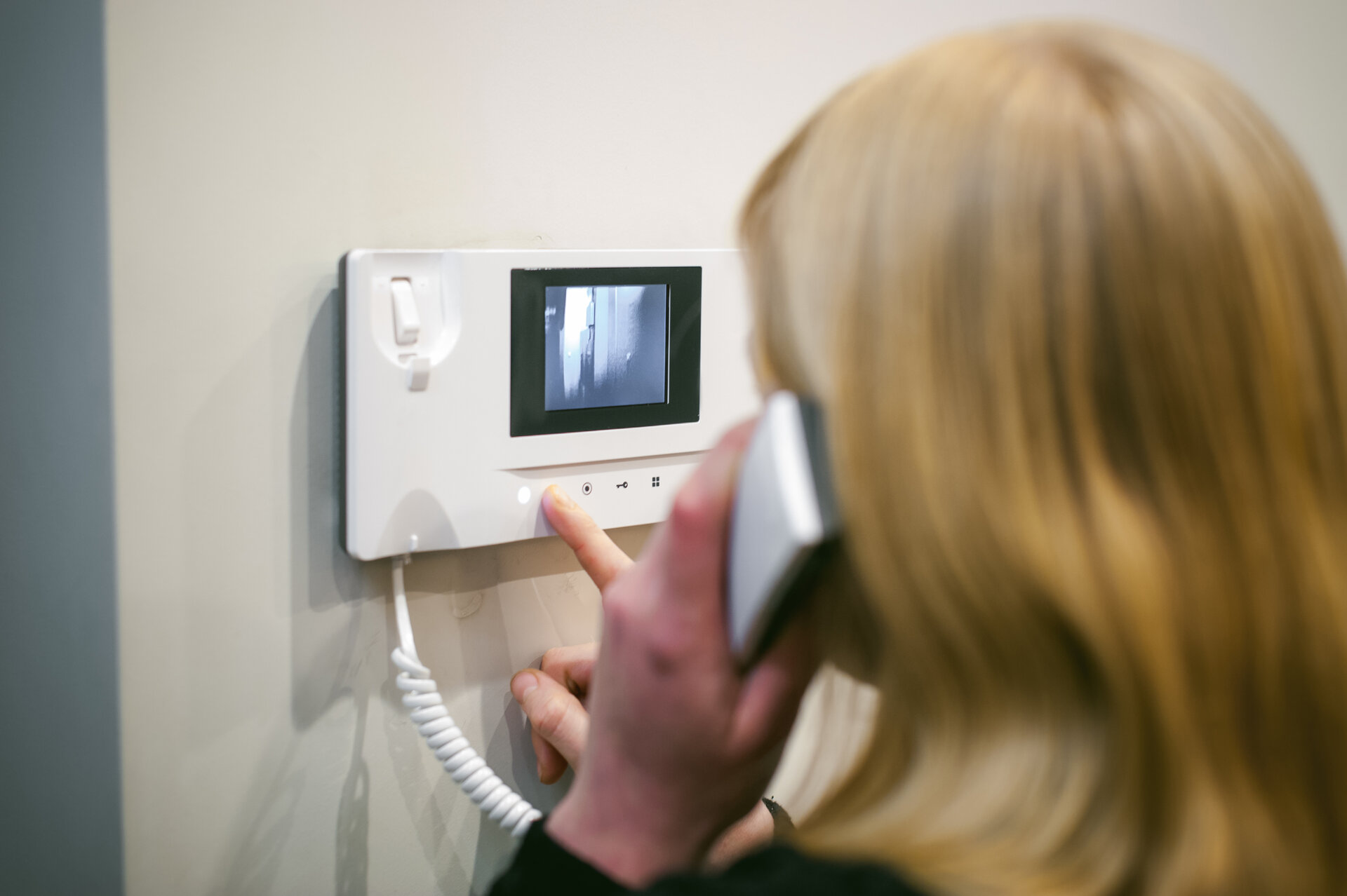 Blonde Frau beantwortet einen Intercom-Anruf, während sie das Telefon an ihr Ohr hält