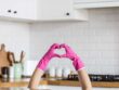 Hände mit Handschuhen formen ein Herz vor einer Küche