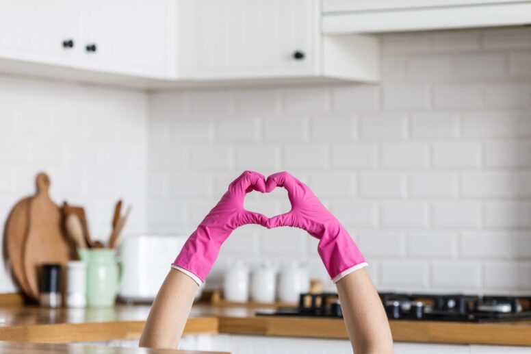 Hände mit Handschuhen formen ein Herz vor einer Küche